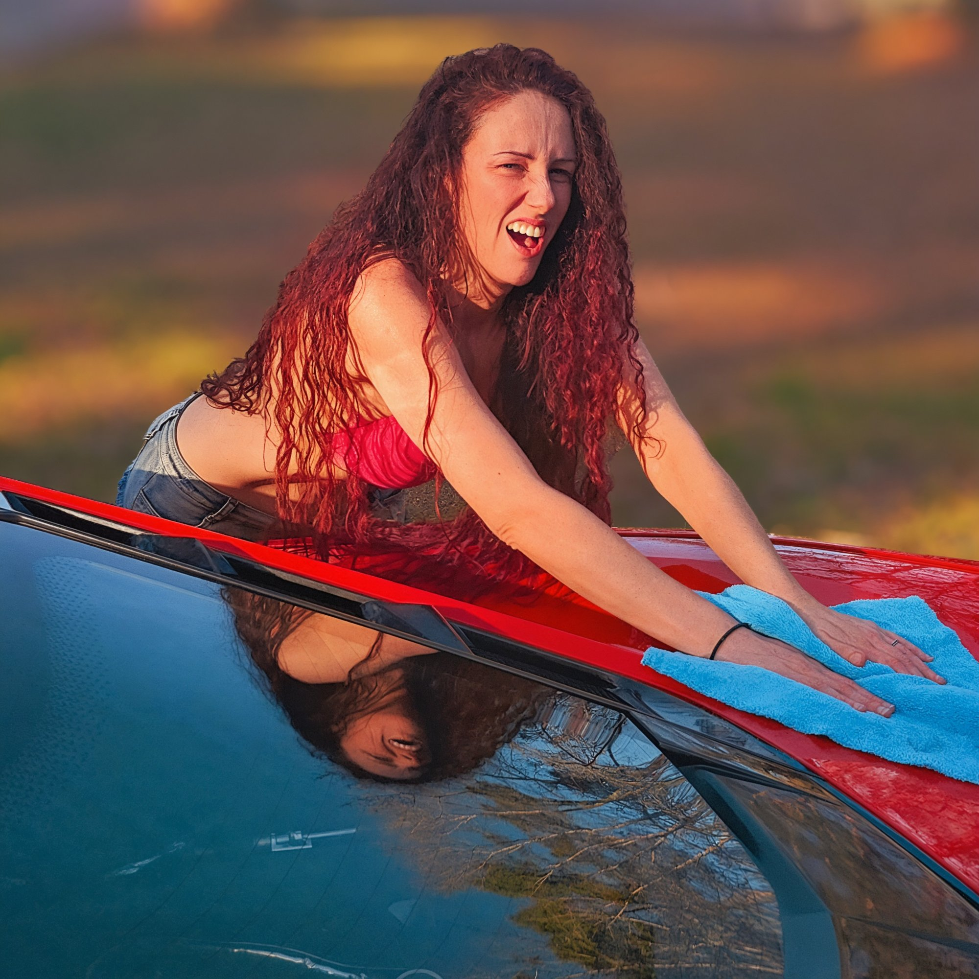 Alice laughing while washing a red sports car at golden hour
